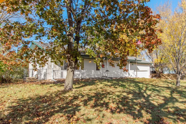 A large maple in autumn color over a front lawn and white house, the kind of yard where tree trimming in Glen Rock may be needed